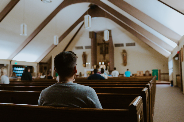 A Male Student Sitting in the Pews in the Back of a Church